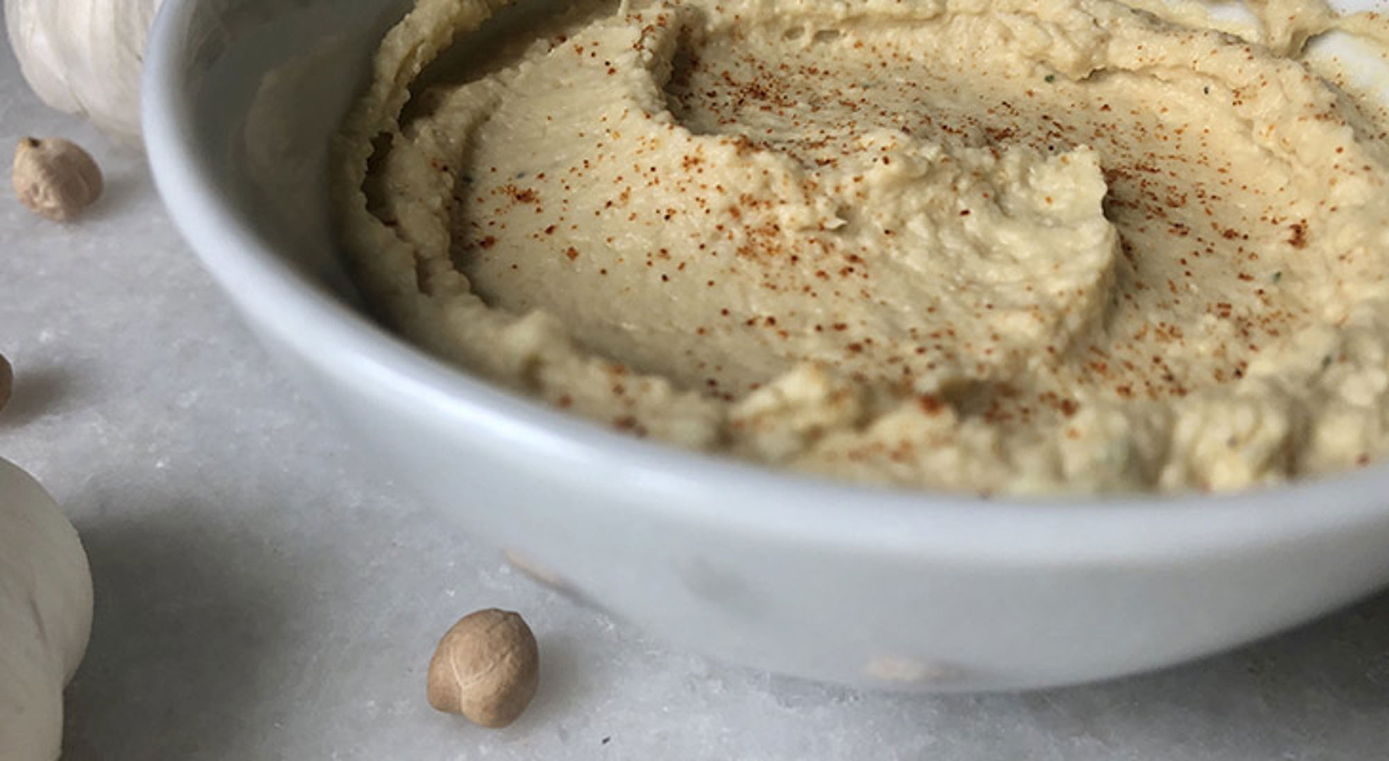 Kom hummus in een witte kom, bestrooid met paprikapoeder.