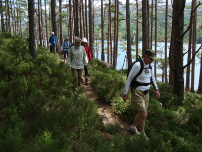 Wandelaars op een bospad langs een meer tijdens de 21-daagse route door Verenigd Koninkrijk en Ierland.