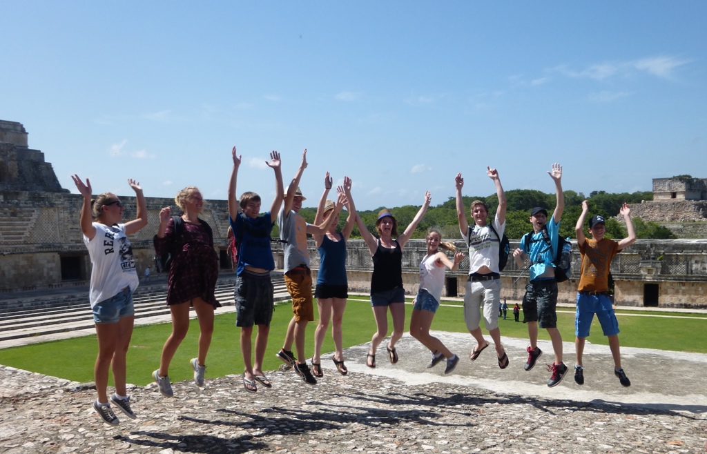 Groep reizigers springt juichend bij een Maya-tempelcomplex in Mexico tijdens een familiereis.