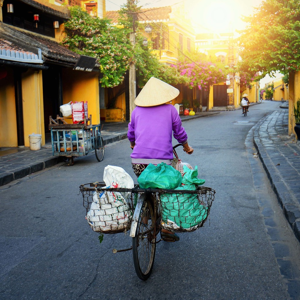 Fietser met Vietnamese hoed in sfeervolle straat in Hoi An, Vietnam.