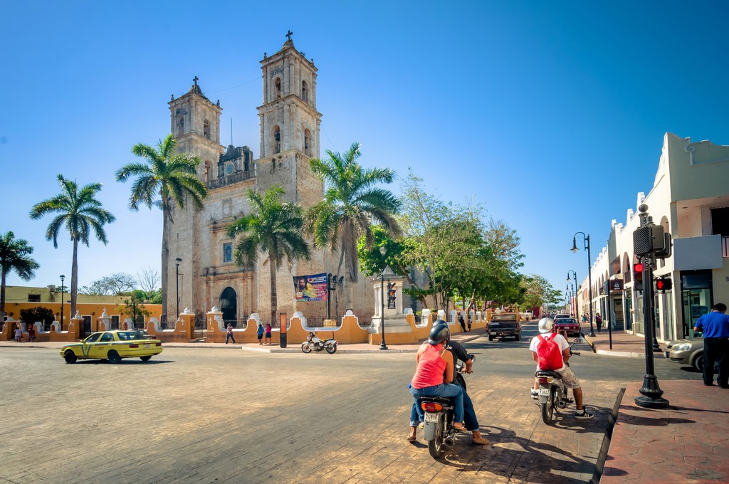 Straatbeeld in Mexico met koloniale kerk, palmbomen en scooters, onderdeel van Familiereis Mexico hoogtepunten.