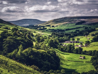 Groene heuvels en vallei met boerderijen langs een kronkelende weg op de route Verenigd Koninkrijk & Ierland.
