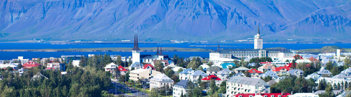 Skyline van Reykjavik met Hallgrímskirkja, kleurrijke huizen en bergen op de achtergrond.