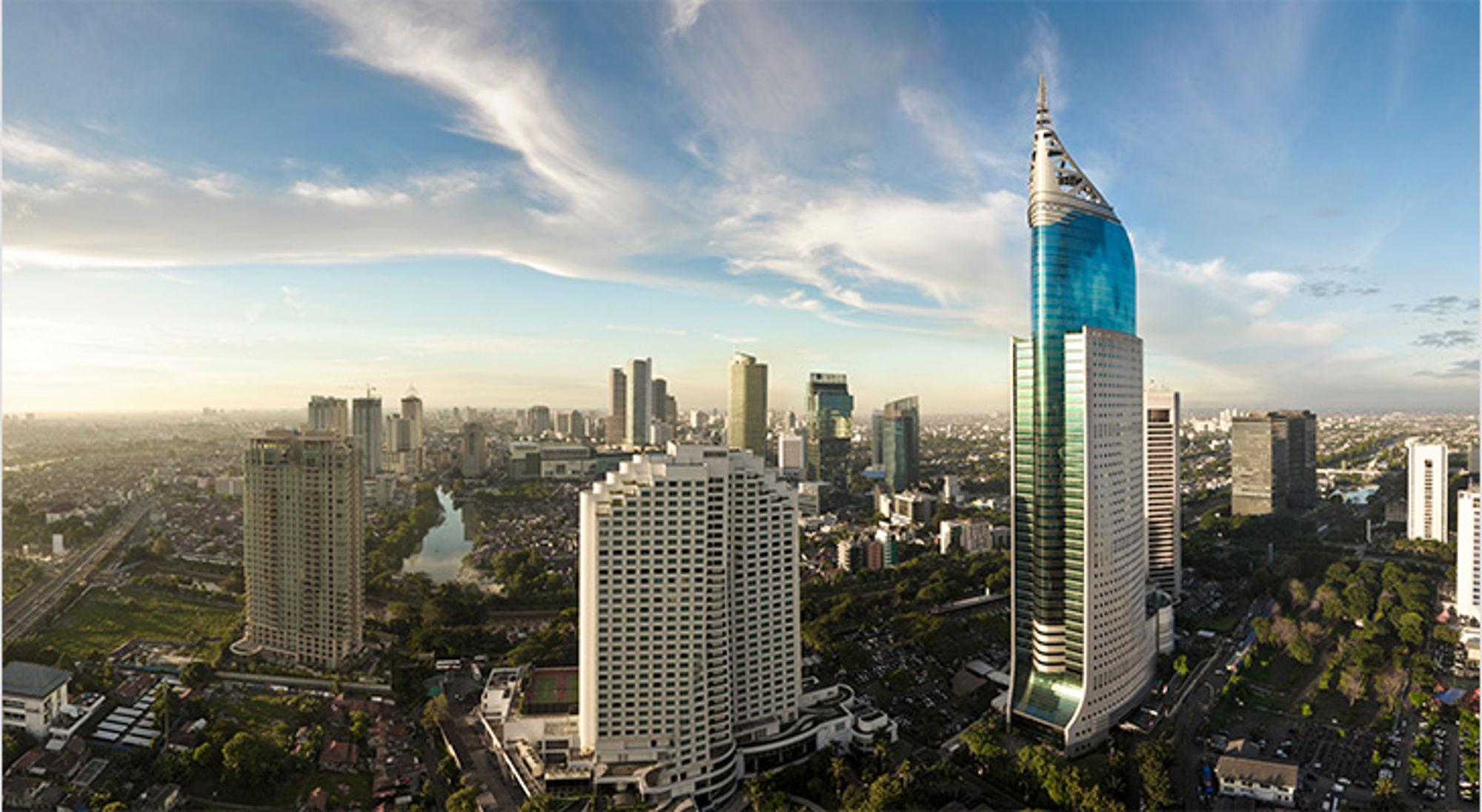 Skyline van Jakarta met moderne wolkenkrabbers en de Wisma 46-toren onder een blauwe lucht.