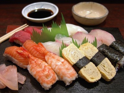 Assortiment sushi met zalm, garnalen, tonijn en omelet op een bord, met sojasaus en eetstokjes.