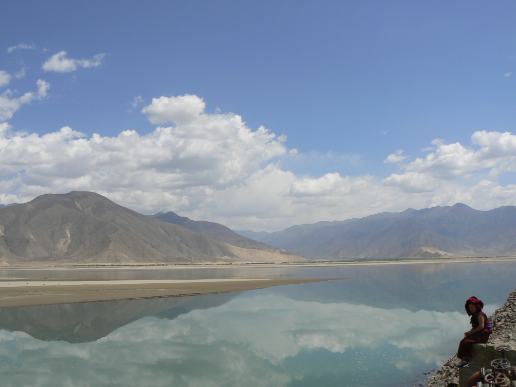 Berglandschap in Tibet met spiegelend meer en wolkenlucht, tijdens groepsrondreis Tibet en Nepal.