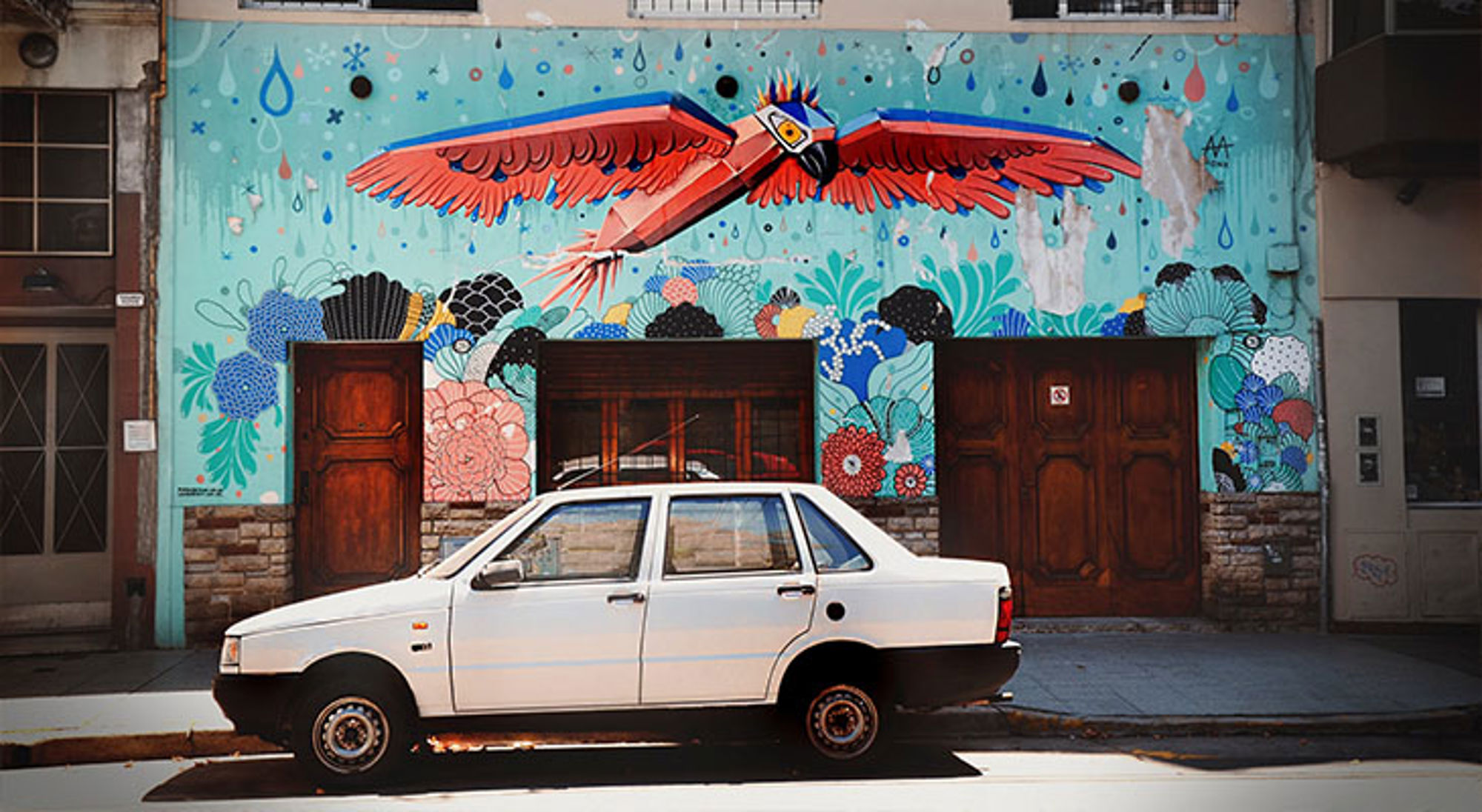 Street art Buenos Aires Witte auto geparkeerd voor kleurrijke muurschildering met vliegende vogel en bloemen.