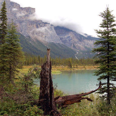 Berglandschap met turquoise meer en dennenbomen in Canada West, met wolken rond de rotswanden.