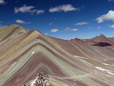 Gekleurde Rainbow Mountain (Vinicunca) in Peru met wandelaars op de bergkam onder een blauwe lucht.