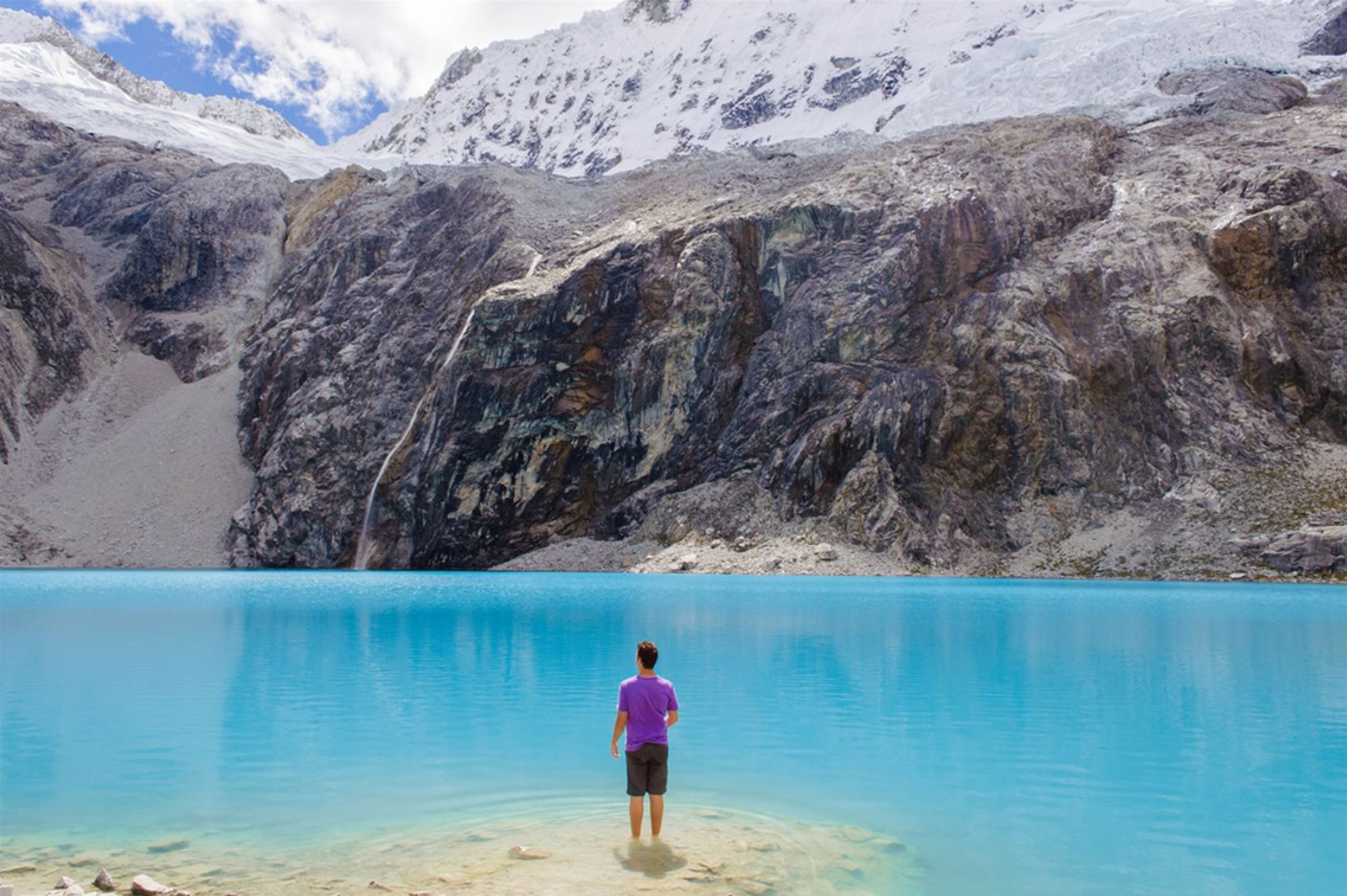 Man staat aan de oever van een turquoise bergmeer met besneeuwde Andesbergen op de achtergrond in Peru.