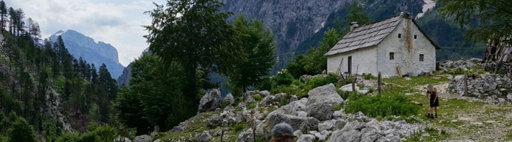 Wandelen in de bergen van Kosovo langs een bergdorp met stenen huisjes en uitzicht op groene valleien.
