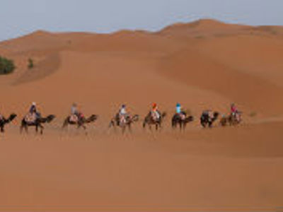 Karavaan met kamelen en reizigers door de zandduinen van de Sahara in Marokko.