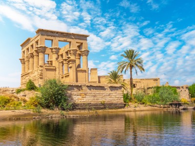 Tempel van Philae bij Aswan aan de Nijl, met palmbomen onder een blauwe lucht.
