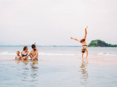 Gezin speelt in zee op een strand in Thailand tijdens de Route Thailand, met kind dat een handstand doet.