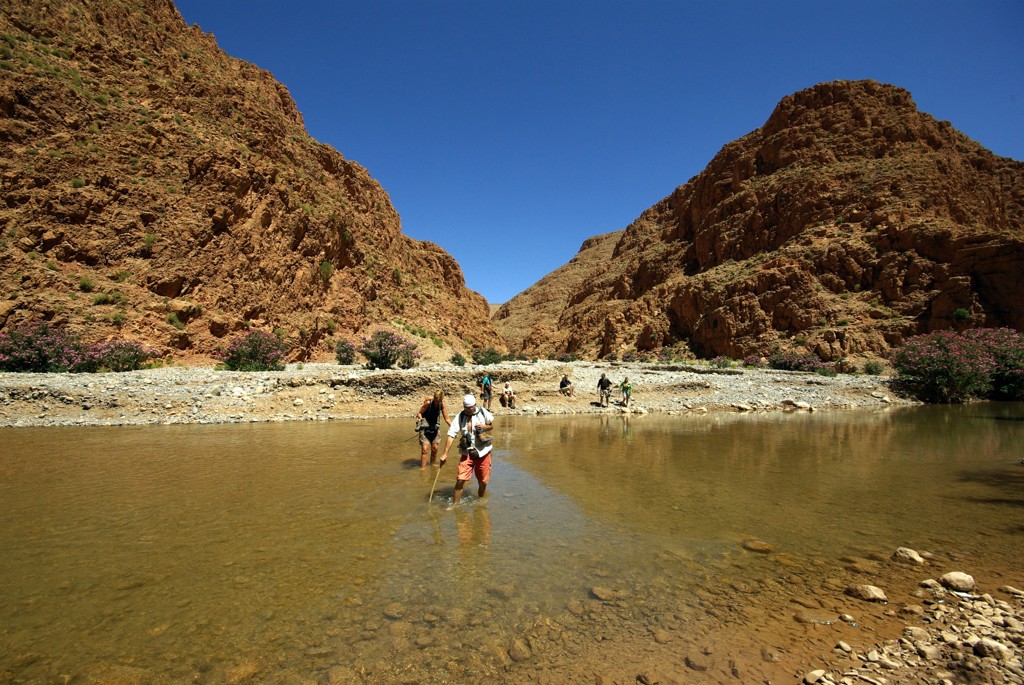 Wandelaars steken een rivier over in een rotsachtige kloof in Marokko tijdens de groepsrondreis Chill & Adventure.