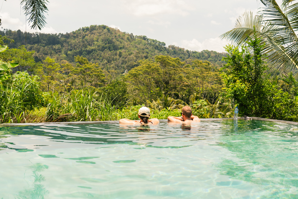 Twee reizigers ontspannen in een infinitypool met uitzicht op de groene jungleheuvels van Bali, Indonesië.