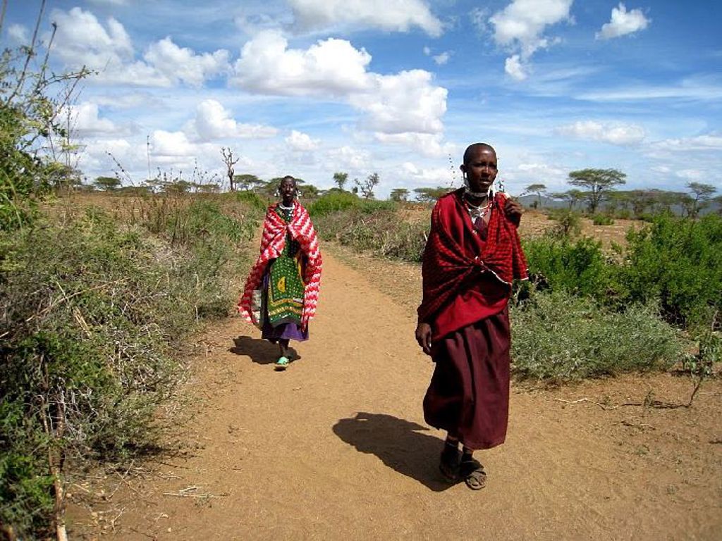 Masai lopen over een zandpad door de savanne tijdens een familiereis in Kenia, Tanzania en Zanzibar.