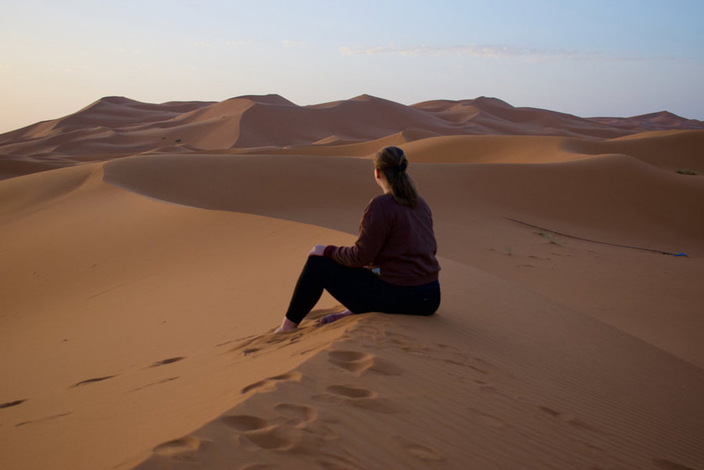 Reiziger zit op een zandduin in de Sahara in Marokko tijdens groepsrondreis Marokko kort.
