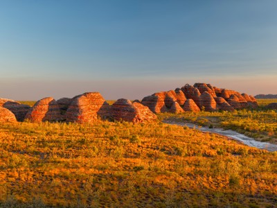 Zonsondergang bij de Bungle Bungle Range in West-Australië, met roodgestreepte rotskoepels en een rivier.