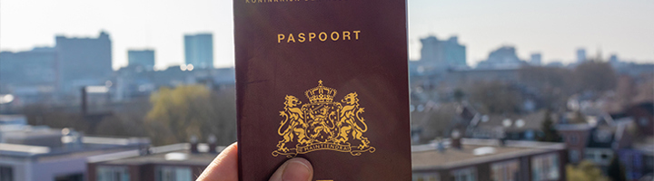 Nederlands paspoort in een hand, met stadsgezicht op de achtergrond.