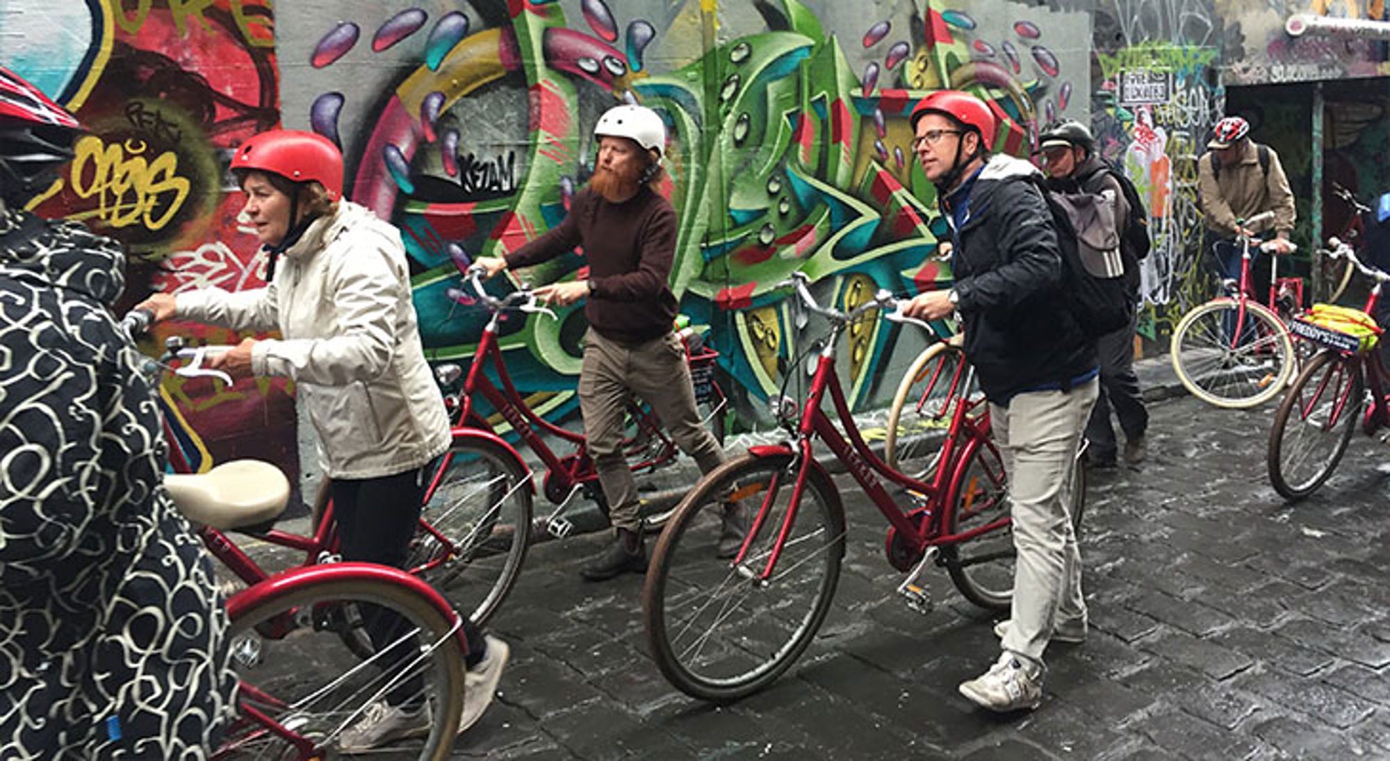 Melbourne Australië Fietstour langs kleurrijke graffiti in een steeg, met deelnemers op rode fietsen en helmen.