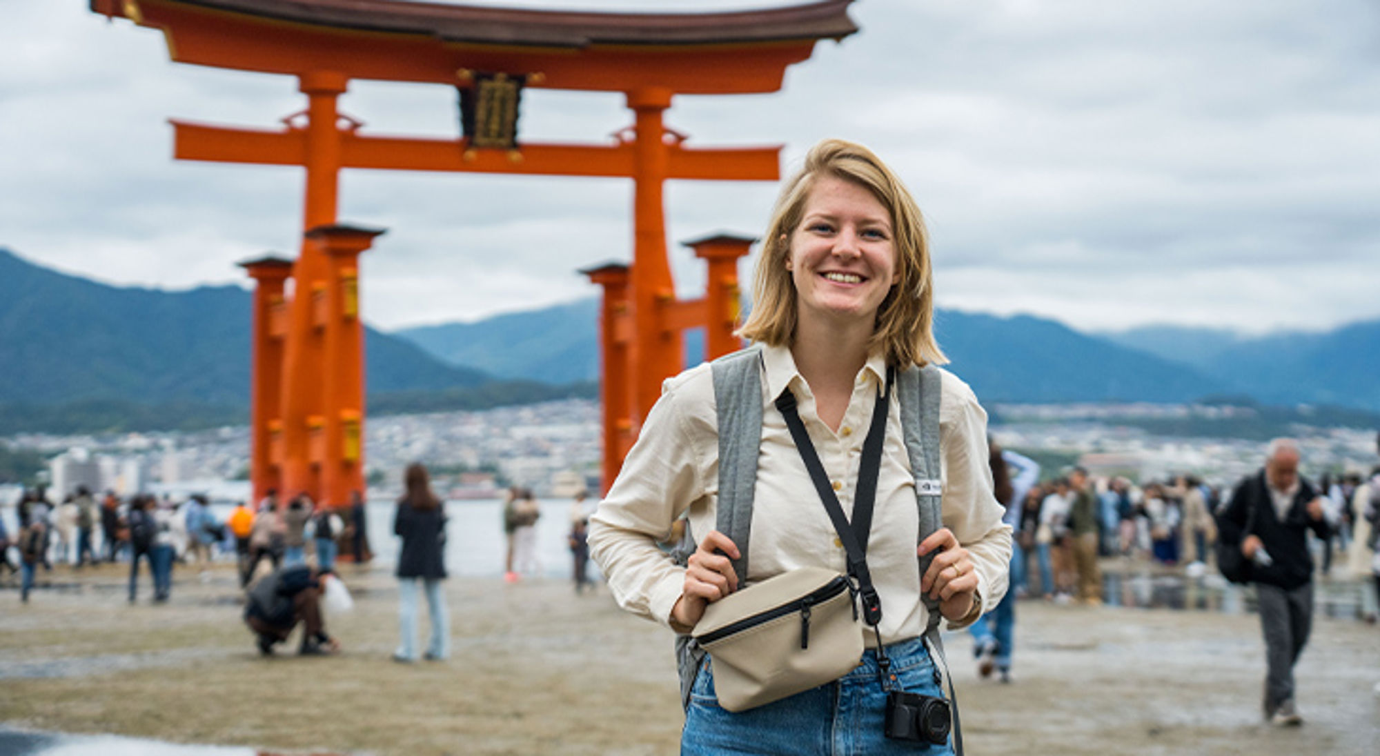 Reiziger poseert bij de rode torii-poort van Itsukushima Shrine op Miyajima, Japan.