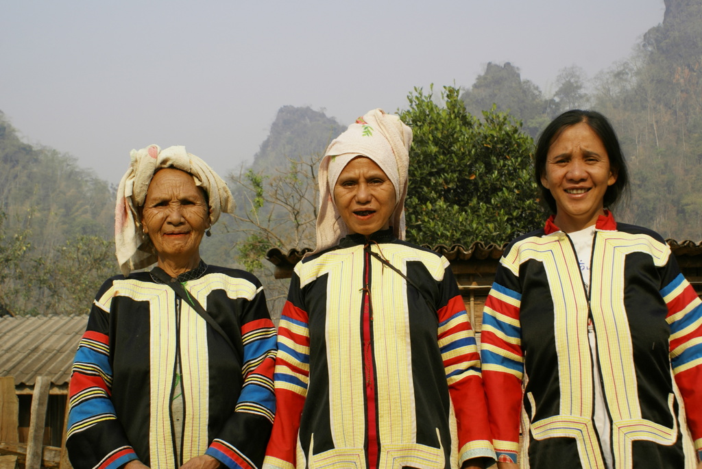 Drie vrouwen in traditionele kleding in Noord-Thailand, met bergen op de achtergrond.