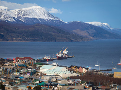 Uitzicht op Ushuaia met haven en zeilboten, met besneeuwde bergen op de achtergrond.