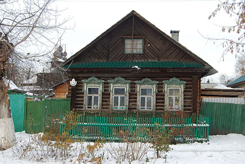 Traditioneel houten huis in Rusland met sierlijke raamkozijnen en sneeuw in de tuin.