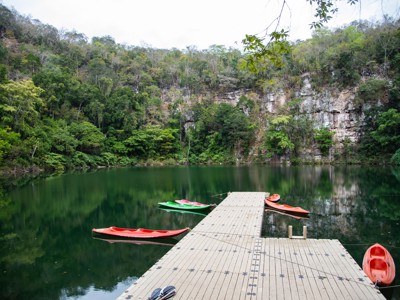 Kajaks aan een steiger bij een groene cenote in Mexico, omringd door jungle en rotswanden.