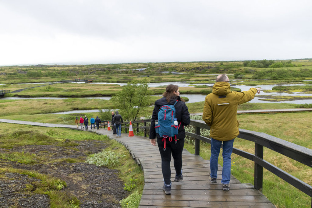 Wandelaars op houten vlonderpad door groen landschap met riviertjes tijdens groepsrondreis IJsland.