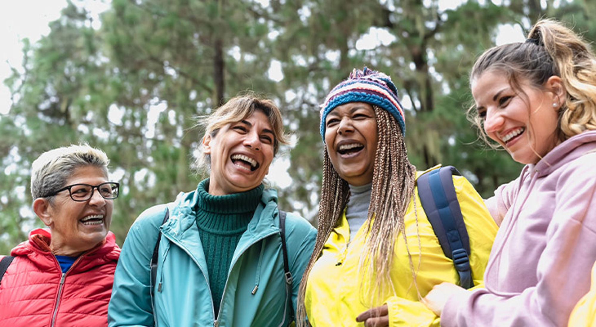 Vier vrouwen lachen tijdens een wandeling in het bos.