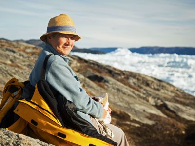 Reiziger pauzeert op rotsen met uitzicht op drijvend ijs langs de kust van Groenland.