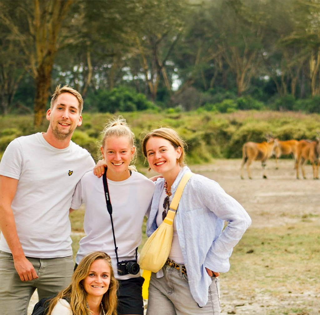 Jonge reizigers op groepsrondreis Kenia & Tanzania, poserend in de natuur met grazende dieren op de achtergrond.