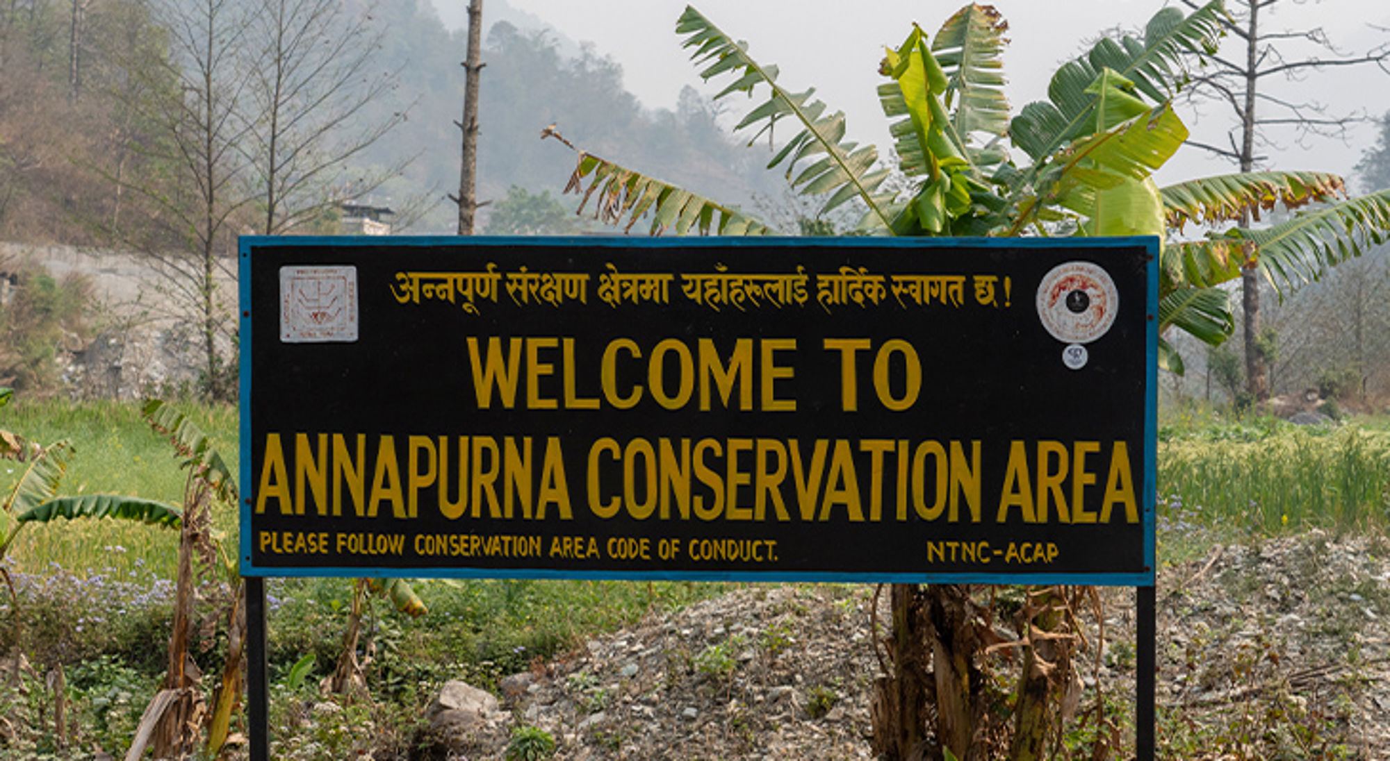 Annapruna gebied Nepal Welkomsbord bij Annapurna Conservation Area in Nepal, met bergen en bananenplanten op de achtergrond.