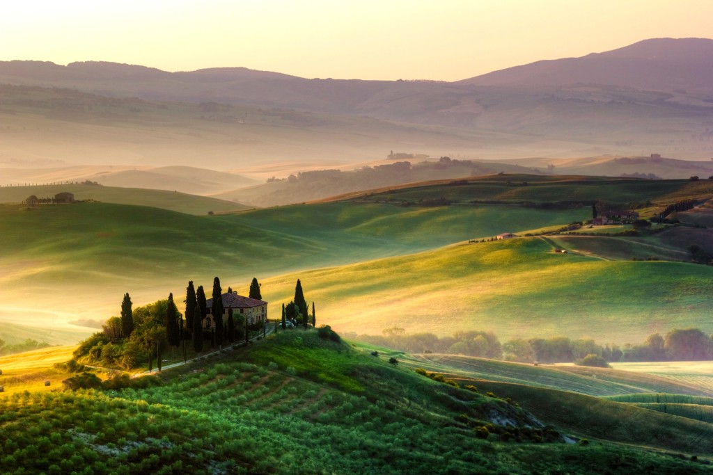 Glooiende heuvels met cipressen en boerderij bij zonsopkomst in Toscane, Italië.