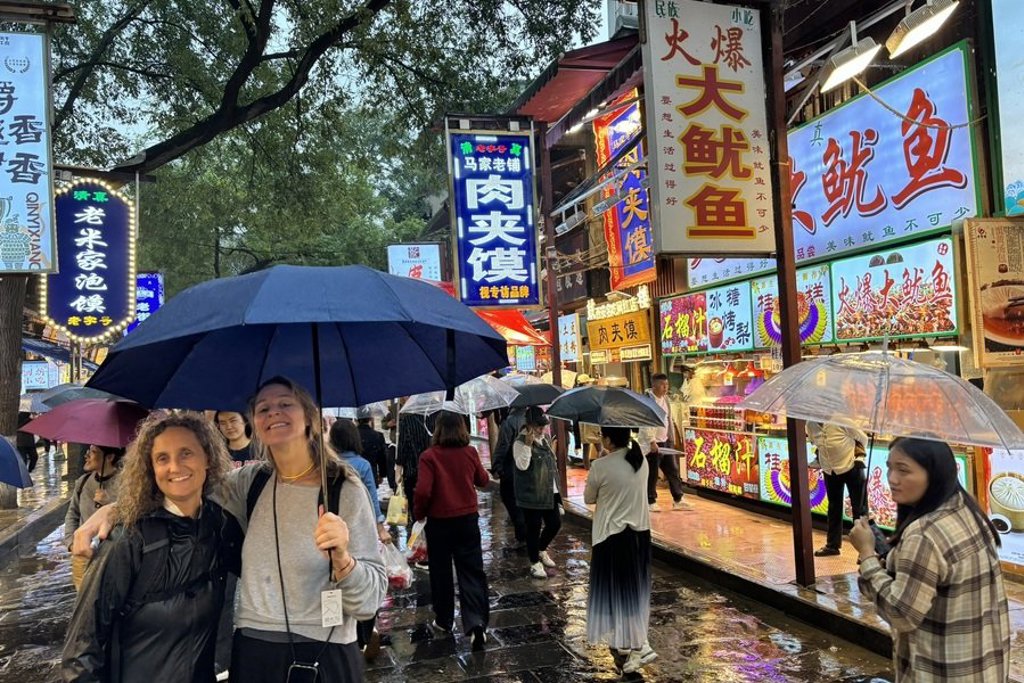 Reizigers met paraplu op een verlichte avondmarkt met foodstands in China tijdens groepsrondreis China.