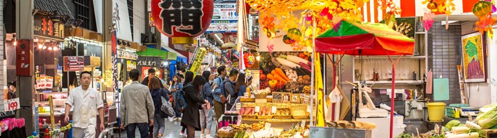 Drukke overdekte Kuromon Ichiba Market in Osaka met marktkramen vol verse groenten en fruit.