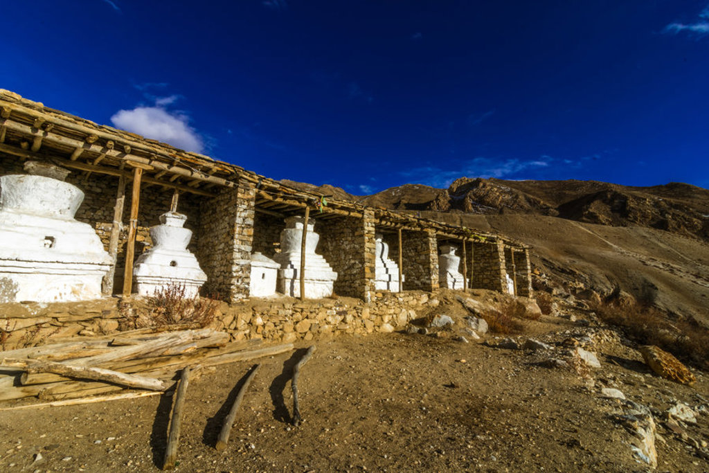 Witte boeddhistische chortens bij een klooster in Ladakh, met ruige bergen onder een diepblauwe lucht.
