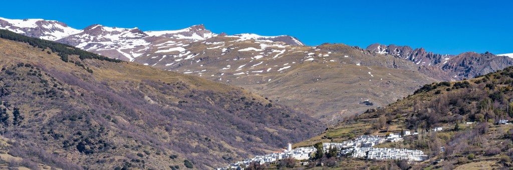 Berglandschap van de Sierra Nevada bij Granada met besneeuwde toppen en een wit bergdorp in de vallei.