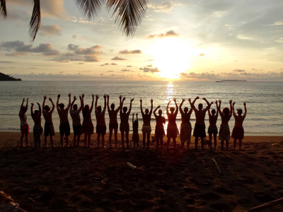Groep reizigers met opgeheven armen op het strand bij zonsondergang in Costa Rica.