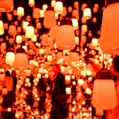 Gloeiende lampeninstallatie bij teamLab in Tokio, met bezoekers tussen honderden hangende lichtobjecten.