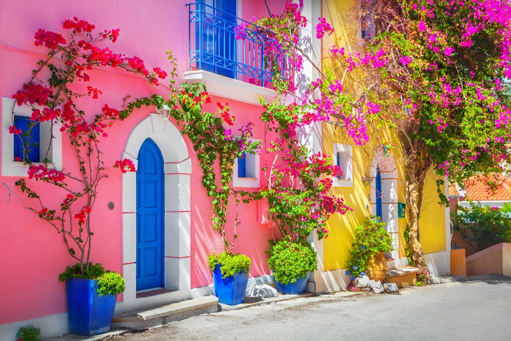Kleurrijke Griekse straat met roze en gele huizen, blauwe deuren en bougainvillea in bloei tijdens 22-35ers reis Griekenland.