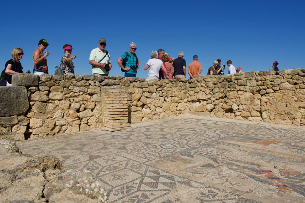 Reizigers bekijken mozaïekvloer bij een archeologische site tijdens een premium groepsrondreis door Marokko.