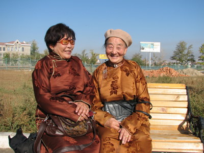 Twee vrouwen in traditionele Mongoolse kleding op een bankje, route Mongolië 23 dagen.