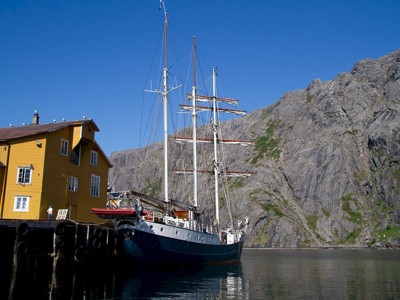 Zeilschip bij de kade in een vissersdorp op de Lofoten, Noorwegen, met steile rotsbergen op de achtergrond.
