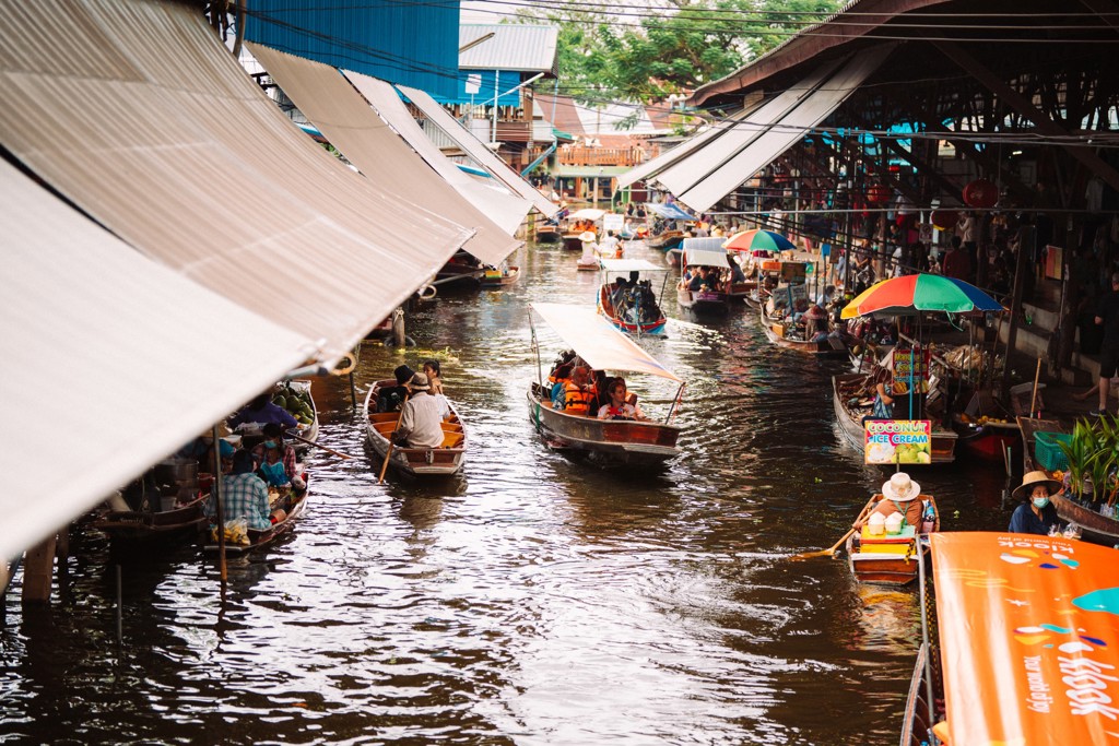 Drukke drijvende markt in Thailand met boten vol koopwaar onder overkappingen, tijdens familiereis Noord en Zuid.