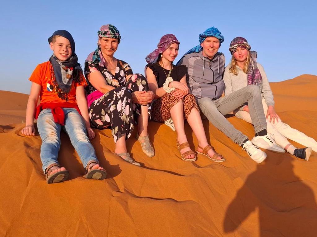Gezin met sjaals zit op zandduinen in de Marokkaanse woestijn tijdens een familiereis Marokko.