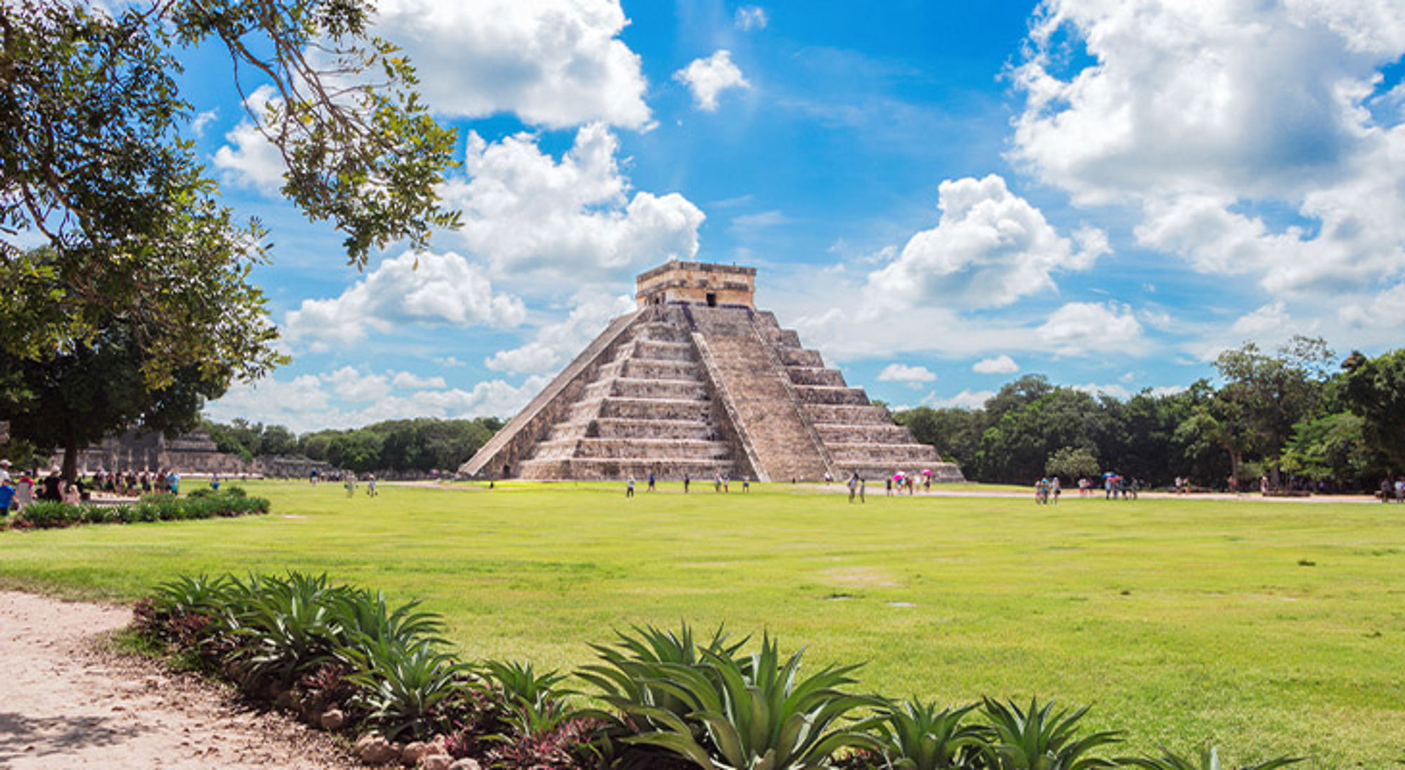 Chichén Itzá Piramide van Kukulcán in Chichén Itzá, Mexico, met bezoekers op het grasveld onder een blauwe lucht.