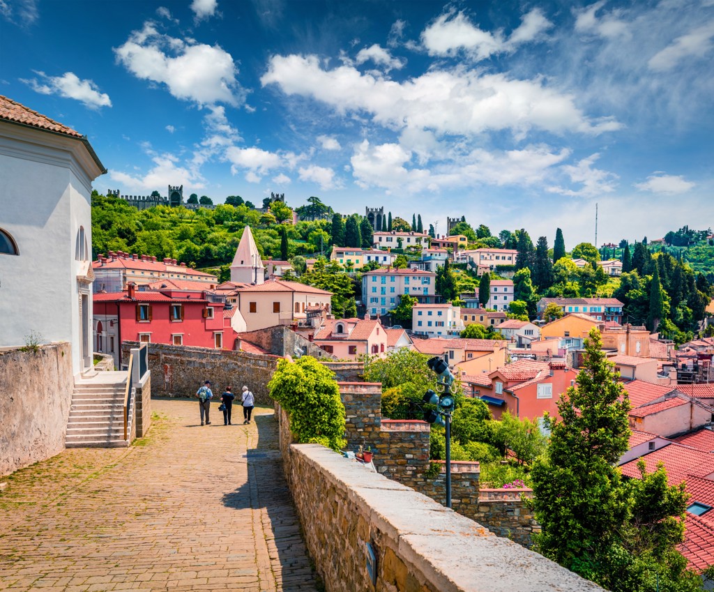 Uitzicht over Piran in Slovenië met kleurrijke huizen en heuvels onder een blauwe lucht.